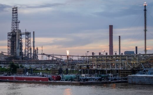A large industrial refinery complex next to a river with a sunset backdrop.