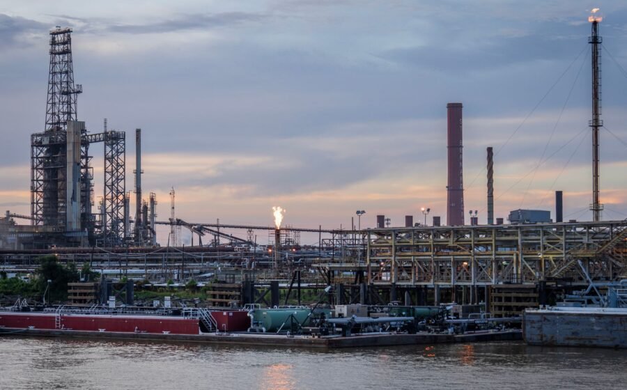 A large industrial refinery complex next to a river with a sunset backdrop.