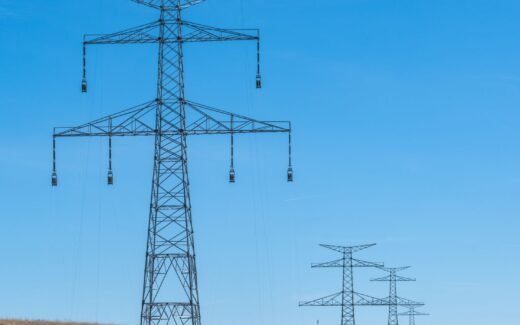 Blue sky over transmission towers on a rural landscape, symbolizing energy distribution.
