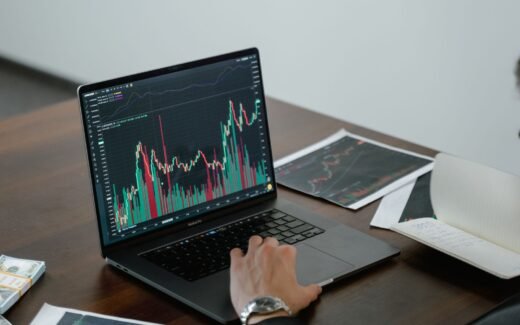 Laptop displaying financial market charts beside printed graphs.