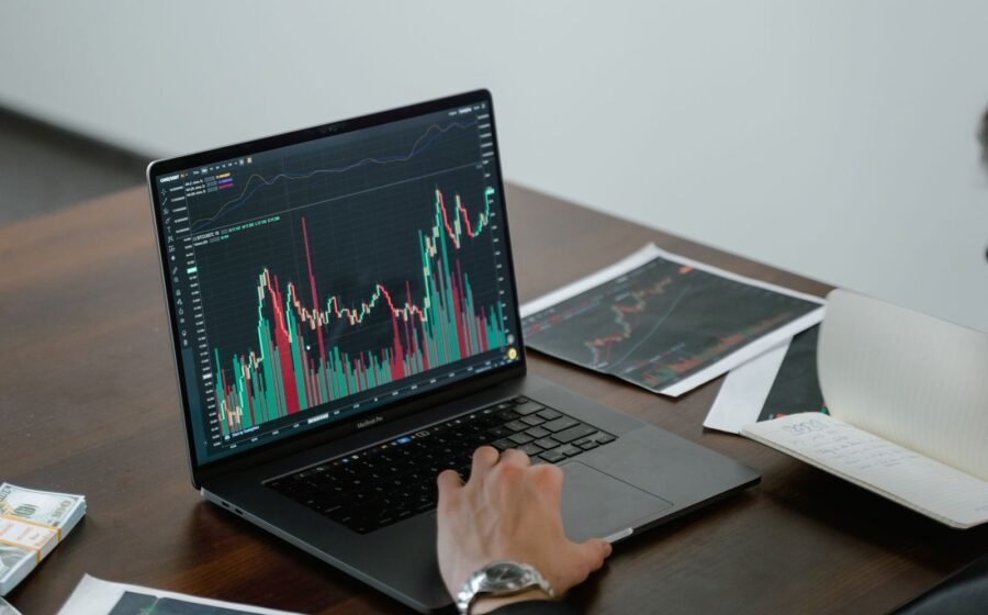 Laptop displaying financial market charts beside printed graphs.
