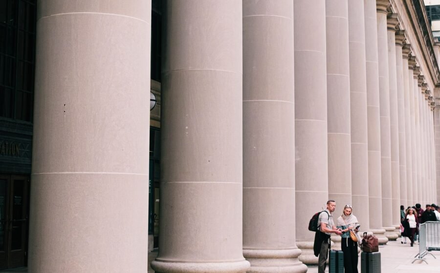 Two travelers stand beside large columns in Chicago, capturing the essence of urban exploration and architectural beauty.